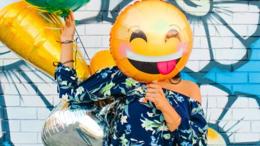 Person holding a smiley face balloon in front of their face.