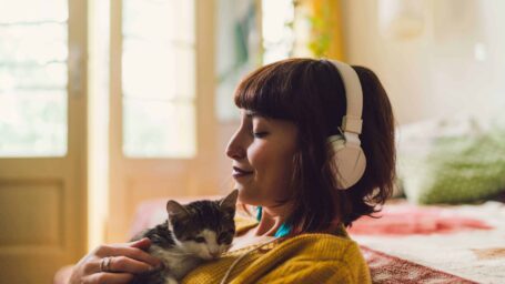 Woman holding kitten while wearing headphones